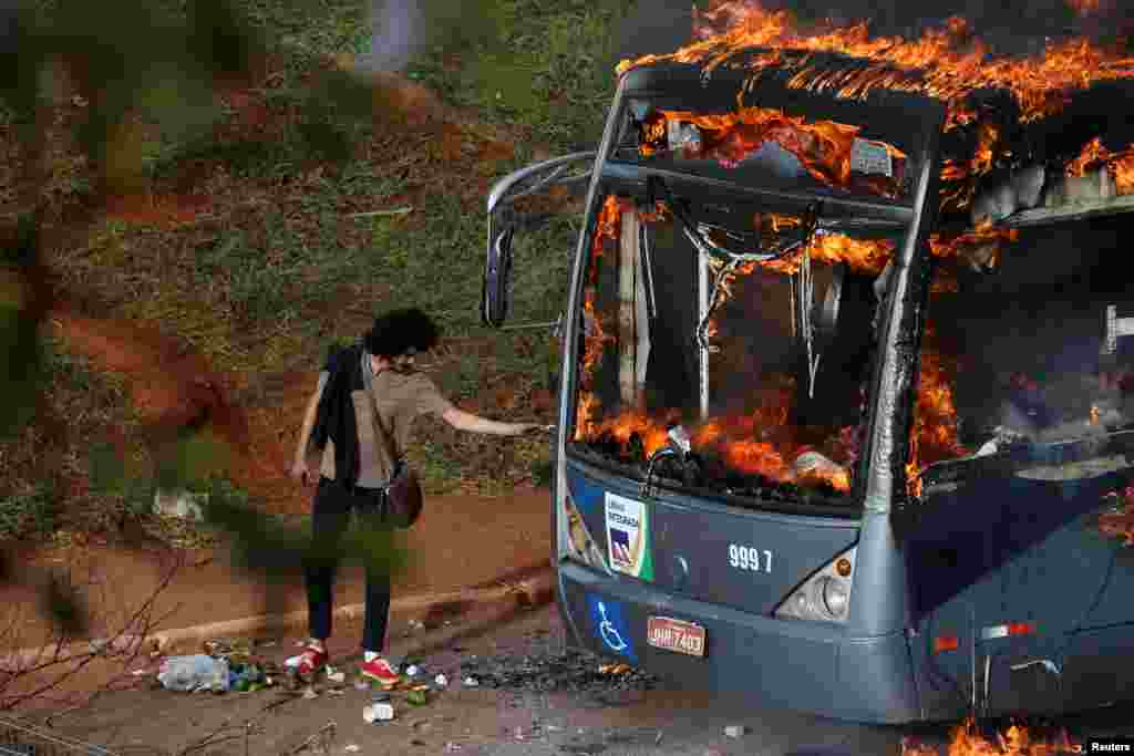 A man lights up his cigarette with the flames of a bus burned by anti-government demonstrators during a protest against the constitutional amendment PEC 55, which limits public spending, in front of Brazil&#39;s National Congress in Brasilia, Dec. 13, 2016.