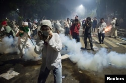 Muslim hardline protesters cover their faces as police fire tear gas during a protest against Jakarta's incumbent governor Basuki Tjahaja Purnama, an ethnic Chinese Christian running in the upcoming election, Nov. 4, 2016.