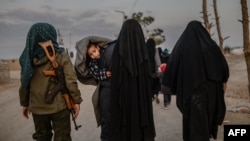 Veiled women, reportedly wives and members of the Islamic State, walk under the supervision of a female fighter from the Syrian Democratic Forces (SDF) at al-Hol camp in al-Hasakeh governorate in northeastern Syria, Feb. 17, 2019.