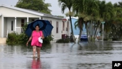 FILE - A woman walks near her flooded neighborhood in Davie, Florida, June 7, 2017. With Hurricane Irma bearing down on Florida, data shows that across the peninsula's 38 coastal counties, just 42 percent of homes in potential hazards zones are insured against flood damage.