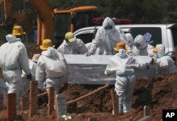 Petugas mengenakan APD menurunkan peti jenazah korban COVID-19 untuk dimakamkan di bagian khusus pemakaman Pedurenan guna menampung lonjakan kematian selama wabah virus corona di Bekasi, Jawa Barat, Senin, 26 Juli 2021. (AP)
