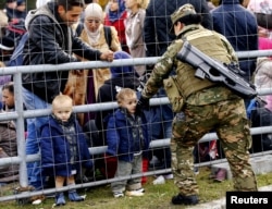 A member of the Slovenian army talks to migrants waiting at the Austrian border near the village of Sentilj, Slovenia, Oct. 25, 2015.