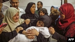 The mother of a Leila al-Ghandour (C), a Palestinian baby of 8 months who according to Gaza's health ministry died of tear gas inhalation during clashes in East Gaza the previous day, holds her at the morgue of al-Shifa hospital in Gaza City on May 15, 20