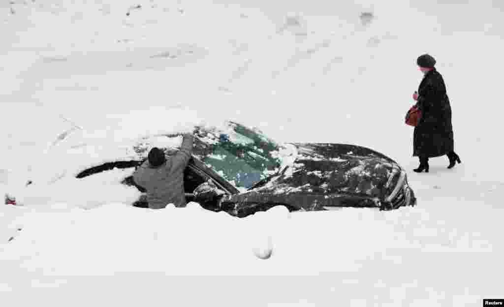 A man clears snow from a car during a snowfall in Moscow, Russia.