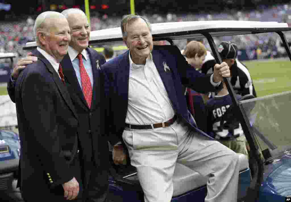 Former President George H. W. Bush, right, former Secretary of State James Baker, left, and Houston Texans owner Bob McNair pose together before an NFL football game against the Buffalo Bills in Houston, November 4, 2012.