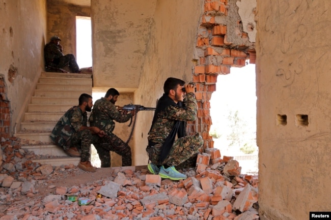 FILE - Kurdish YPG fighters take up positions inside a damaged building as they monitor the movements of Islamic State fighters who are stationed in Ghwayran neighborhood in Hasaka city, Syria, July 22, 2015.