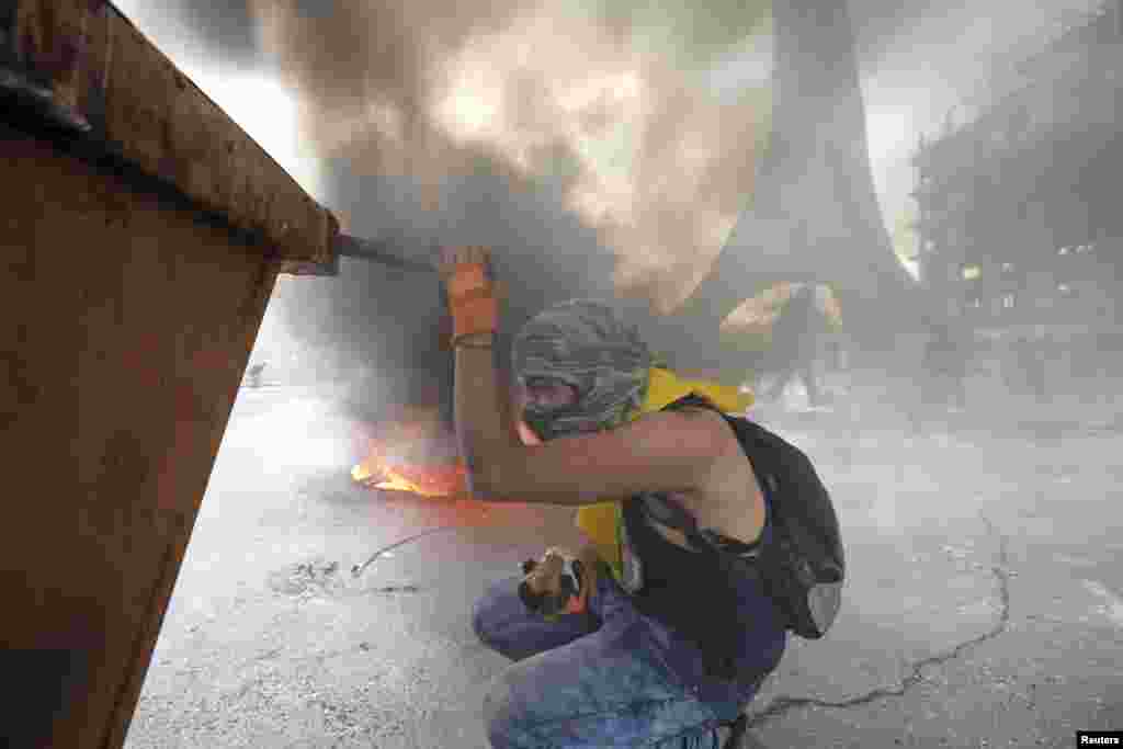 Smokes rises from a fire as a Palestinian protester takes cover during clashes with Israeli troops near the Jewish settlement of Beit El, near the West Bank city of Ramallah.