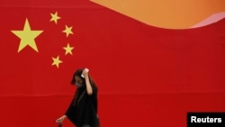 FILE - A woman wearing a mask walks past a wall painted with China's national flag in central Beijing.