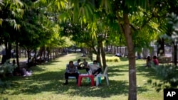 FILE - Police officers sit in the shade of a tree on a hot, humid day at a public park in Yangon, Myanmar, March 17, 2016.