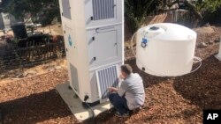 Ted Bowman, design engineer with Tsunami Products, installs a unit in homeowner Don Johnson's backyard in Benicia, Calif., Sept. 28, 2021. The recent invention can make water out of the air and in parched California, some homeowners are already buying the devices. (AP Photo)