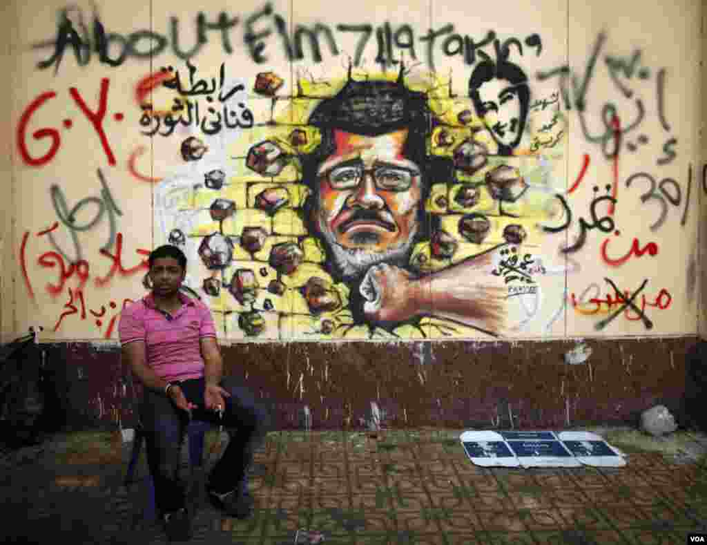 A protester, opposing Egypt&#39;s President Mohamed Morsi, sits next to graffiti depicting Morsi on a wall in Cairo July 2, 2013.