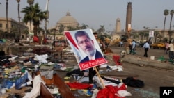 Seorang warga Mesir membawa poster Presiden terguling Mohammed Morsi di antara sisa-sisa kamp protes di Lapangan Nahda, Giza, Kairo, Mesir (15/8).