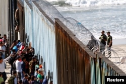 Migrants, part of a caravan of thousands trying to reach the U.S., look through the border fence between Mexico and the United States, in Tijuana, Mexico, Nov. 14, 2018.