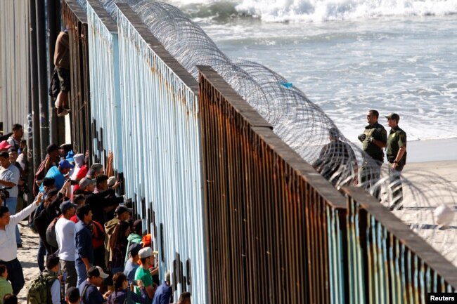 Migrants, part of a caravan of thousands trying to reach the U.S., look through the border fence between Mexico and the United States, in Tijuana, Mexico, Nov. 14, 2018.