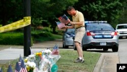Rich Lindgren, de Virginia Beach, coloca banderas estadounidenses en un monumento improvisado en el borde de un cordón policial frente a un edificio municipal que fue el escenario de un tiroteo.