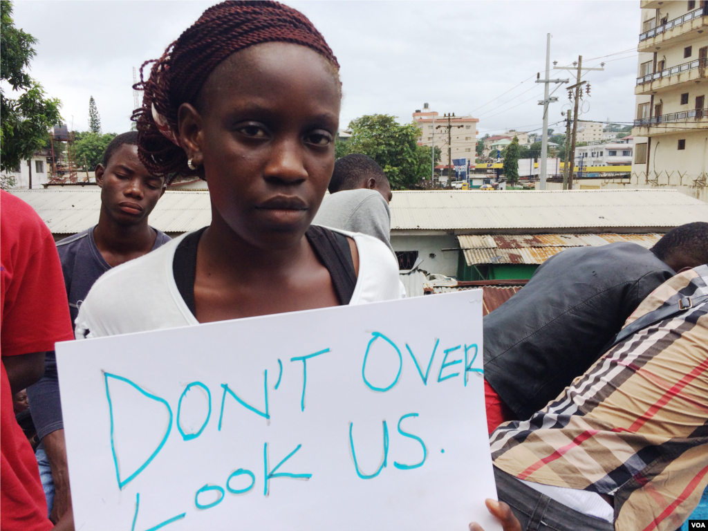 Gloria Maya Terrick segura um cartaz pedindo ao governo que permita aos estudantes envolverem-se na luta contra o Ébola, à porta da sede de uma Organização Não Governamental, Monróvia, Libéria, Set. 29, 2014. (Benno Muchler/VOA) 
