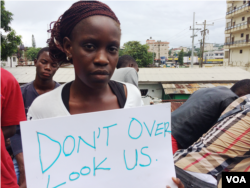 Gloria Maya Terrick holds a sign requesting the government to allow the students to help in the fight against Ebola, outside NGO headquarters, in Monrovia, Liberia, Sept. 29, 2014. (Benno Muchler/VOA)
