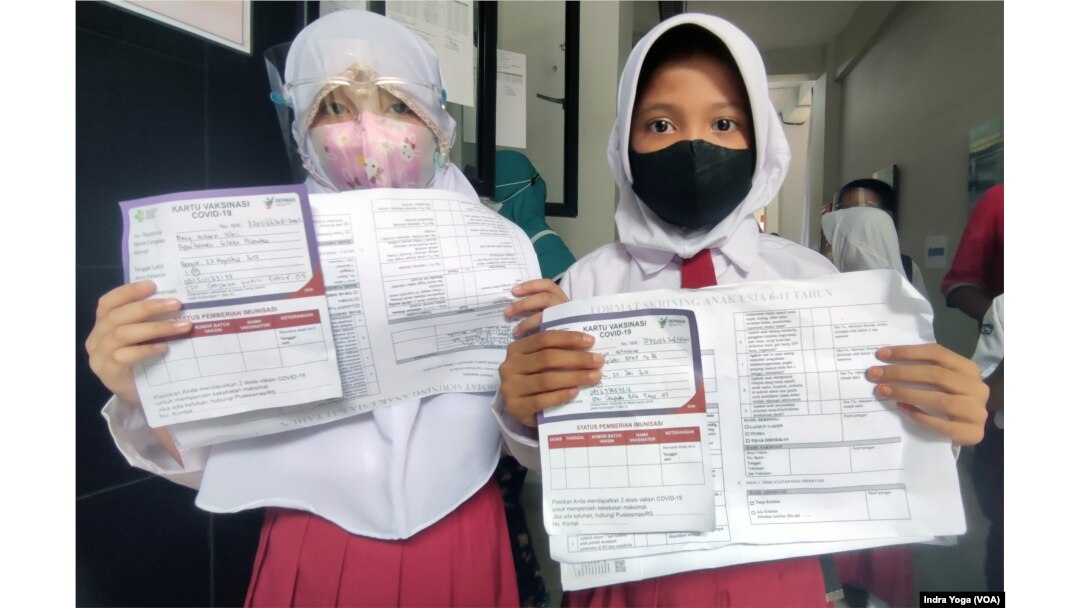 Dua orang siswi menunjukkan kartu registrasi keikutsertaan vaksin untuk anak usia 6 sampai 11 tahun di SD Negeri Cempaka Putih Timur 03. Sebanyak kurang lebih 150 anak berpartisipasi di sekolah dasar tersebut pada 14 Desember 2021. (VOA/Indra Yoga)