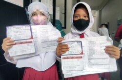 Dua orang siswi menunjukkan kartu registrasi keikutsertaan vaksin untuk anak usia 6 sampai 11 tahun di SD Negeri Cempaka Putih Timur 03. Sebanyak kurang lebih 150 anak berpartisipasi di sekolah dasar tersebut pada 14 Desember 2021. (VOA/Indra Yoga)
