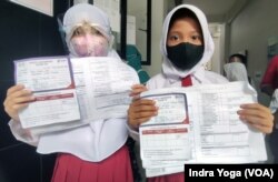 Dua orang siswi menunjukkan kartu registrasi keikutsertaan vaksin untuk anak usia 6 sampai 11 tahun di SD Negeri Cempaka Putih Timur 03. Sebanyak kurang lebih 150 anak berpartisipasi di sekolah dasar tersebut pada 14 Desember 2021. (VOA/Indra Yoga)