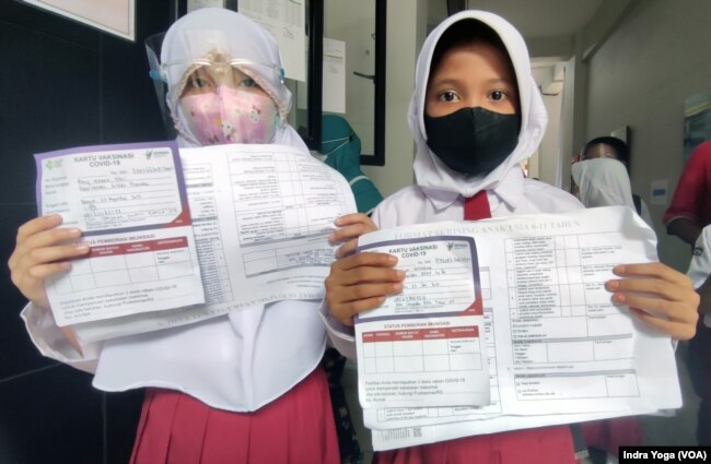 Dua orang siswi menunjukkan kartu registrasi keikutsertaan vaksin untuk anak usia 6 sampai 11 tahun di SD Negeri Cempaka Putih Timur 03. Sebanyak kurang lebih 150 anak berpartisipasi di sekolah dasar tersebut pada 14 Desember 2021. (VOA/Indra Yoga)