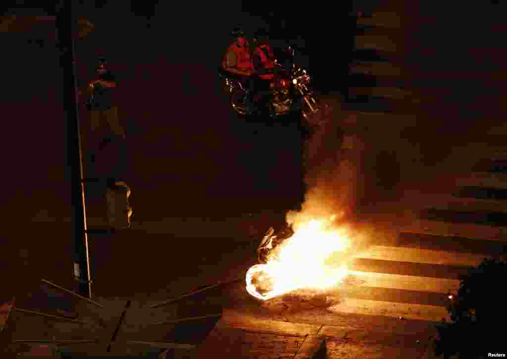 Motorcycle taxi drivers stand next to a burning motorbike set ablaze by anti-government demonstrators, Altamira Square in Caracas, Feb. 26, 2014.&nbsp;