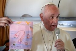 FILE - Pope Francis shows drawings made by children on his flight back to Rome following a visit to the Greek island of Lesbos, April 16, 2016.