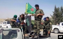 FILE - In this file photo released June 23, 2015, provided by the Kurdish fighters of the People's Protection Units (YPG), which has been authenticated based on its contents and other AP reporting, Kurdish fighters of the YPG sit on their pickup in the town of Ein Eissa, north of Raqqa city, Syria.