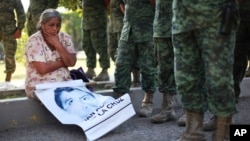 FILE - A woman who identified herself as the mother of missing student Adan Abarajan de la Cruz, 23, sits next to Mexican army soldiers standing in front of the entrance to the 27th Infantry Battalion base in Iguala, Mexico, Dec. 18, 2014.