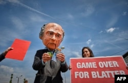 A man wearing a mask depicting FIFA President Sepp Blatter holding Swiss Francs stands next to a woman holding a banner reading "Game over for Blatter" during a protest held in front of the Hallenstadium where the 65th FIFA Congress takes place in Zurich,