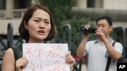 FILE - In this Aug. 1, 2016 photo, a man films Li Wenzu, wife of imprisoned lawyer Wang Quanzhang. She holds a paper that reads "Release Liu Ermin" as she and others stage a protest in Tianjin, China.