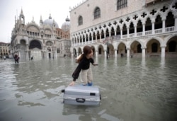 A tourist pushes her floating suitcase in a flooded St. Mark's Square, in Venice, Wednesday, Nov. 13, 2019. The high-water mark hit 187 centimeters late Tuesday, Nov. 12, 2019.