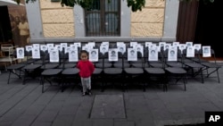 Seorang anak berdiri di depan kursi-kursi kosong dengan potret 43 mahasiswa yang hilang, yang dibuat berderet untuk memperingati sembilan bulan menghilangnya mereka dari Mexico City (27/6). (AP/Marco Ugarte)