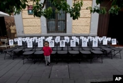 FILE - A child stands before a memorial made up of empty chairs bearing images of 43 missing students, set up to mark the nine-month anniversary of their disappearance, in Mexico City, June 27, 2015.