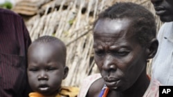 In this photo of Thursday, Jan.12, 2012 a mother waits with her son for emergency food rations from the World Food Program in the town of Gumuruk, 35 kilometers southwest of Pibor, South Sudan. Tens of thousands fled their homes after ethnic violence erup