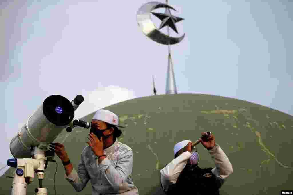 A boarding school student and an official use a telescope and a monocular to view the moon on the roof of Al Musariin mosque to mark the first day of Ramadan in Jakarta, Indonesia.