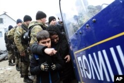 FILE - Macedonian policemen stand guard as a woman and a kid pass from the northern Greek village of Idomeni to southern Macedonia, Nov. 20, 2015.