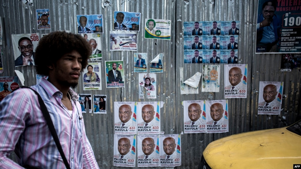 A man walks past a wall filled with campaign posters in the district of Lingwala in Kinshasa, Dec. 18, 2018.