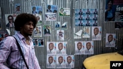 A man walks past a wall filled with campaign posters in the district of Lingwala in Kinshasa, Dec. 18, 2018. 
