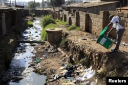 FILE - A student empties a dustbin next to a murky stream near a school in Kenya's Kibera slums in capital Nairobi, Sept. 21, 2015.