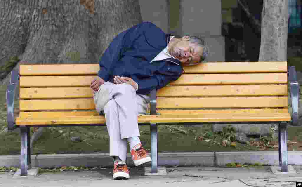 A man takes a nap on a bench at a park in Tokyo, Japan.