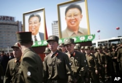 North Korean soldiers walk in the Ryomyong residential area, a collection of more than a dozen apartment buildings, after attending its official opening ceremony, while portraits of the late leaders Kim Il Sung and Kim Jong Il are seen at rear on April 13, 2017.