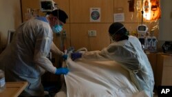 Terapis pernapasan Frans Oudenaar, kiri, dan perawat terdaftar Bryan Hofilena menutupi tubuh pasien COVID-19 dengan selembar kain di Providence Holy Cross Medical Center di Los Angeles, 14 Desember 2021. (Foto: AP)