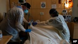 FILE - Respiratory therapist Frans Oudenaar, left, and registered nurse Bryan Hofilena cover a body of a COVID-19 patient with a sheet at Providence Holy Cross Medical Center in Los Angeles, Dec. 14, 2021.