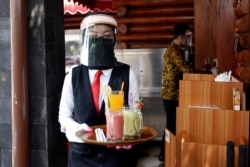 Seorang pelayan restoran mengenakan pelindung dan masker wajah membawa pesanan untuk konsumen di sebuah restoran di tengah pandemi virus corona, 29 Mei 2020. (Foto: Reuters)