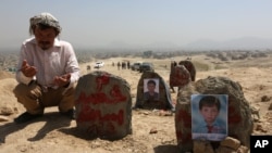 FILE - An Afghan man prays in front graves of victims of a suicide attack, in Kabul, Afghanistan, July 25, 2016. 