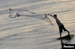 FILE - A man casts a fishing net on the bank of the Mekong river in Phnom Penh.