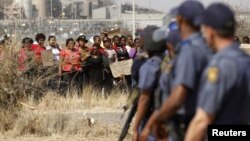 Police look on as women carry placards in protest against the killing of miners by the South African police on Thursday, outside a South African mine in Rustenburg, 100 kilometers northwest of Johannesburg, August 17, 2012.