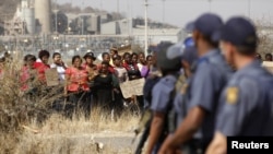 Police look on as women carry placards in protest against the killing of miners by the South African police on Thursday, outside a South African mine 100 kilometers northwest of Johannesburg, August 17, 2012.