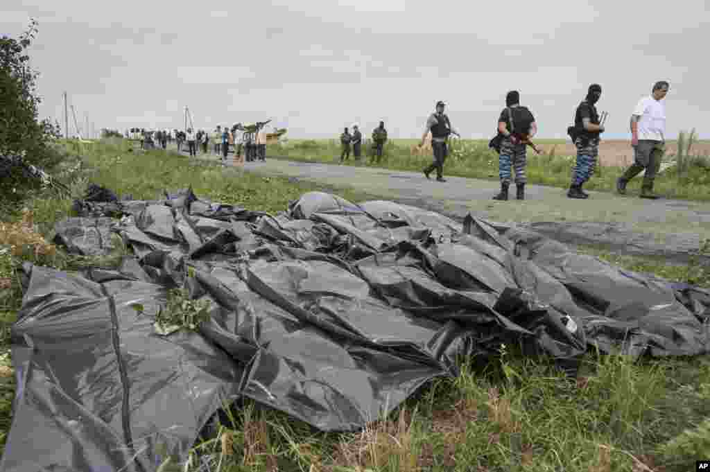 Pro-Russian fighters walk on a road with victims&#39; bodies lying in bags by the side at the crash site of a Malaysia Airlines jet near the village of Hrabove, eastern Ukraine, July 19, 2014.